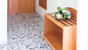 Een hal met een houten deur, een houten bankje met een bloemstuk en een spiegel aan de muur.