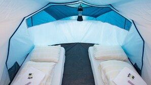 A tent with two beds, each with pillows and a blanket, and a hanging light fixture. - GPtents- Munich Oktoberfest (Munich)