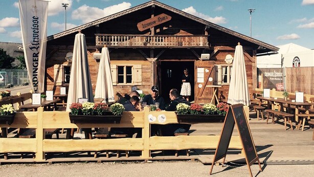 An outdoor seating area with wooden tables and benches, a wooden building with a sign reading "Eringer Biergarten," and a banner with the Eringer logo. - GPtents- Munich Oktoberfest (Munich)