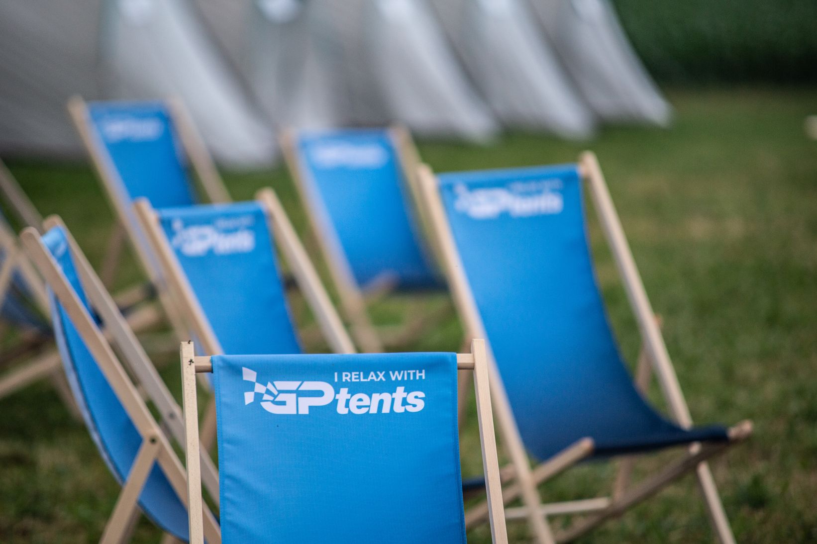A row of blue chairs with a logo and text, arranged outdoors on grass.