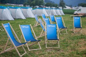 Eine Reihe blauer Liegestühle mit dem Schriftzug 'I RELAX WITH tents', vor einer Kulisse aus Zelten und einem Rasenfeld.