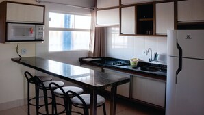 Eine kompakte Küche mit integriertem Mikrowellenherd, Spüle und Kühlschrank. Zwei Barhocker und ein Fenster sorgen für natürliches Licht.