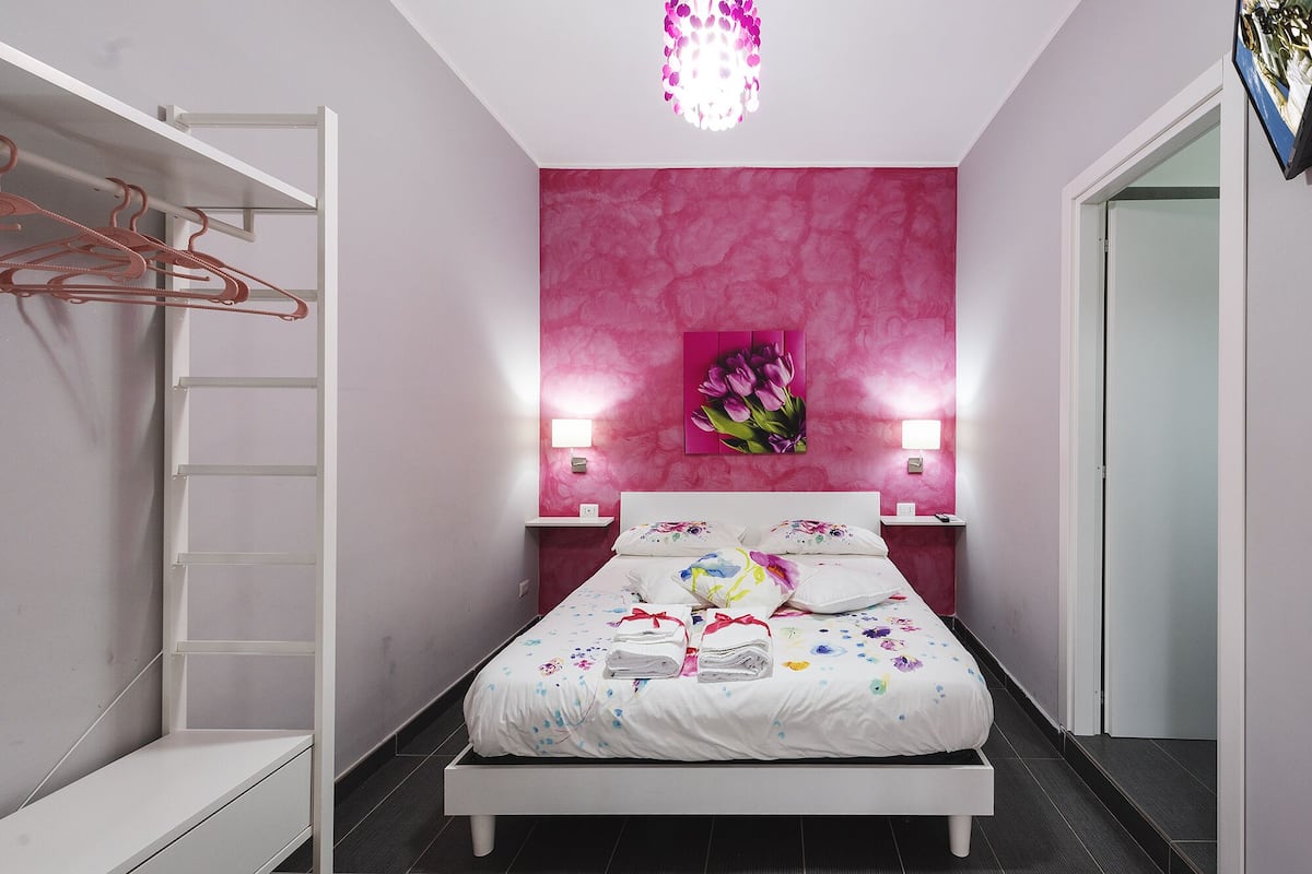 Quarto com cama, guarda-roupa, parede rosa e um candelabro.