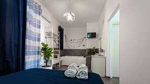 A modern bedroom with a bed, a plant, a hanging light fixture, a bathroom with a bathtub, and a TV mounted on the wall. - Terra Mia (Pompei)
