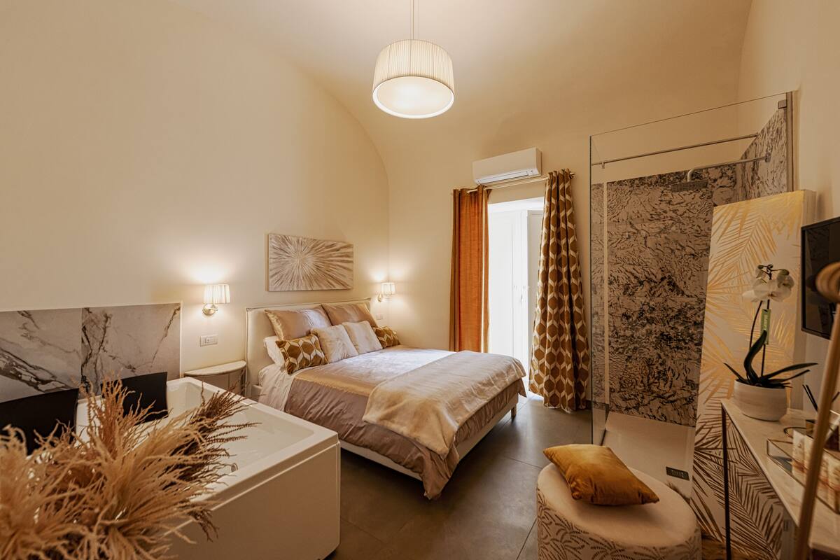 Quarto com cama, mesas de cabeceira, um espelho e um vaso de planta.