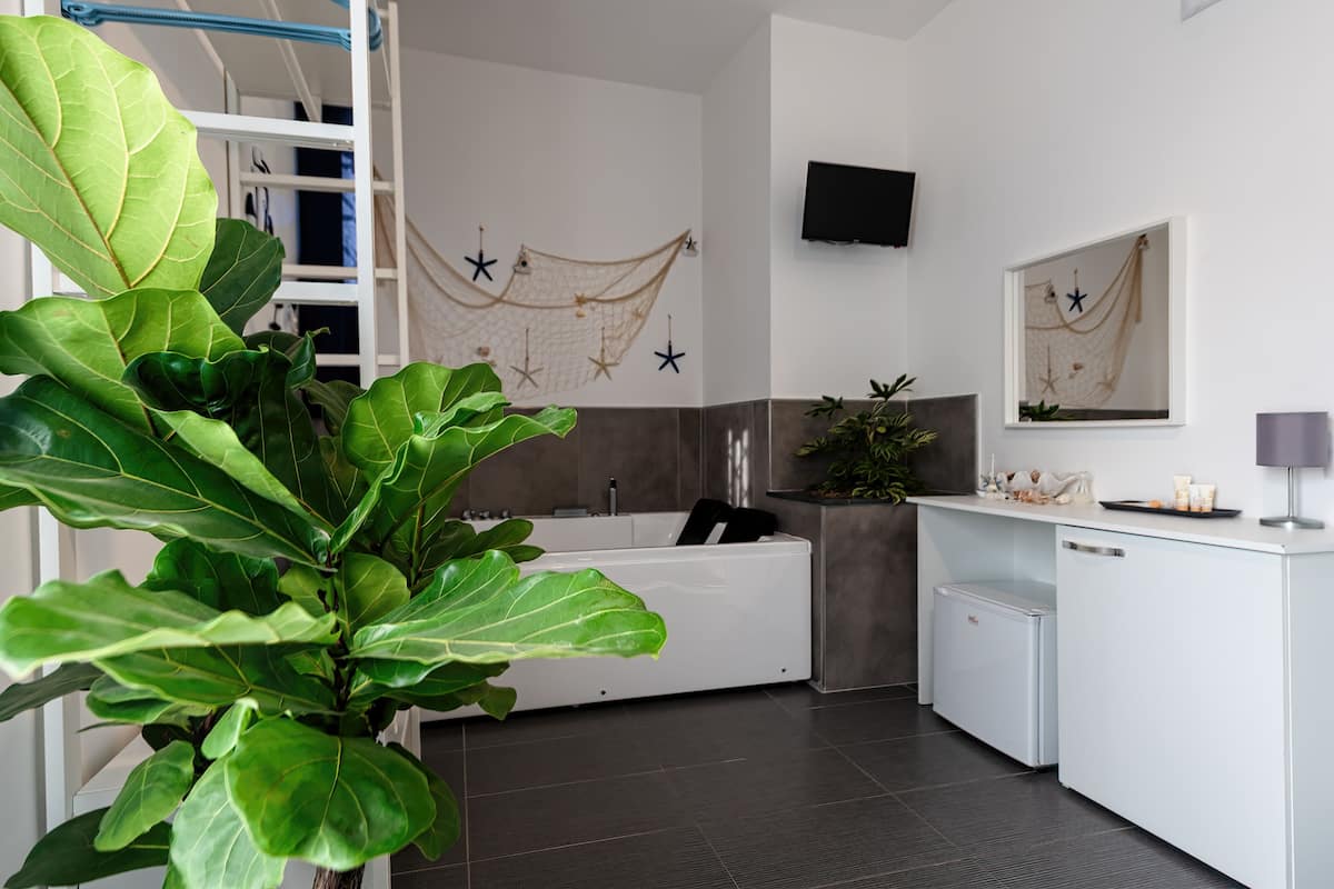 Um banheiro moderno com banheira, chuveiro e pia. Há uma planta verde grande no canto, um porta-toalhas e um espelho sobre a pia.