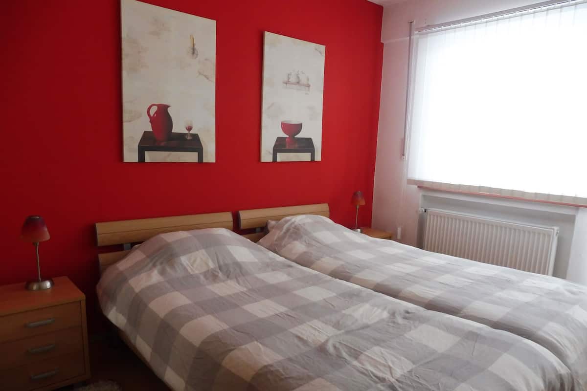 A bedroom with two beds, a red wall, and two paintings.