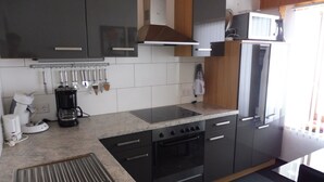 Moderni keittiö, jossa on sisäänrakennettu liesi, uuni ja mikroaaltouuni. Keittiössä on kaappeja, pesuallas ja työtaso, jossa on erilaisia keittiövälineitä.