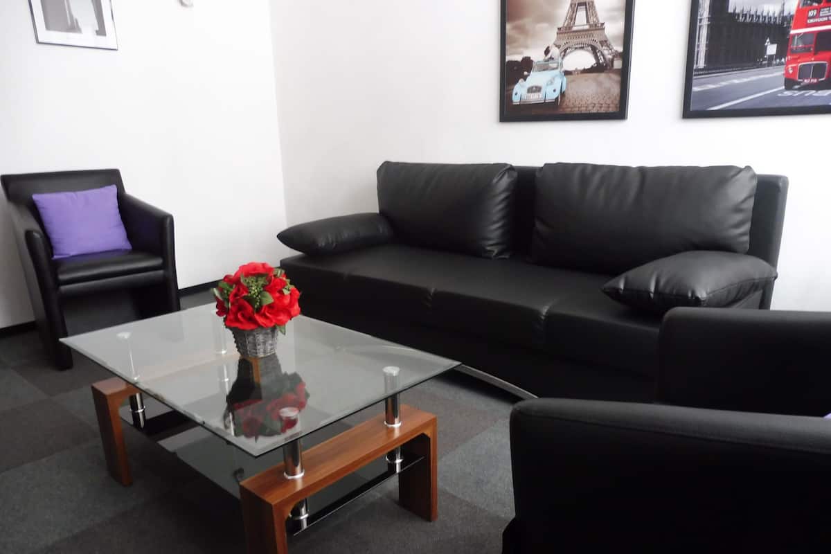 A modern living room with a glass coffee table, black leather sofa, and a purple cushion.