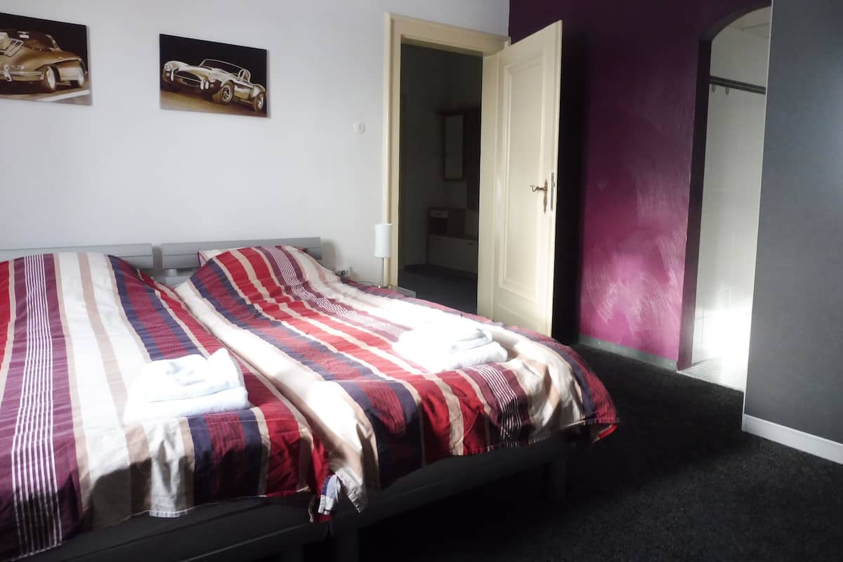 A bedroom with a bed, two wall-mounted pictures, and a door leading to another room.