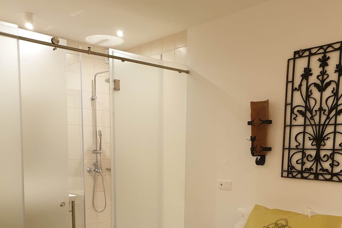 Une chambre moderne avec une douche en verre, un lit recouvert d’un plaid jaune et un élément décoratif mural.