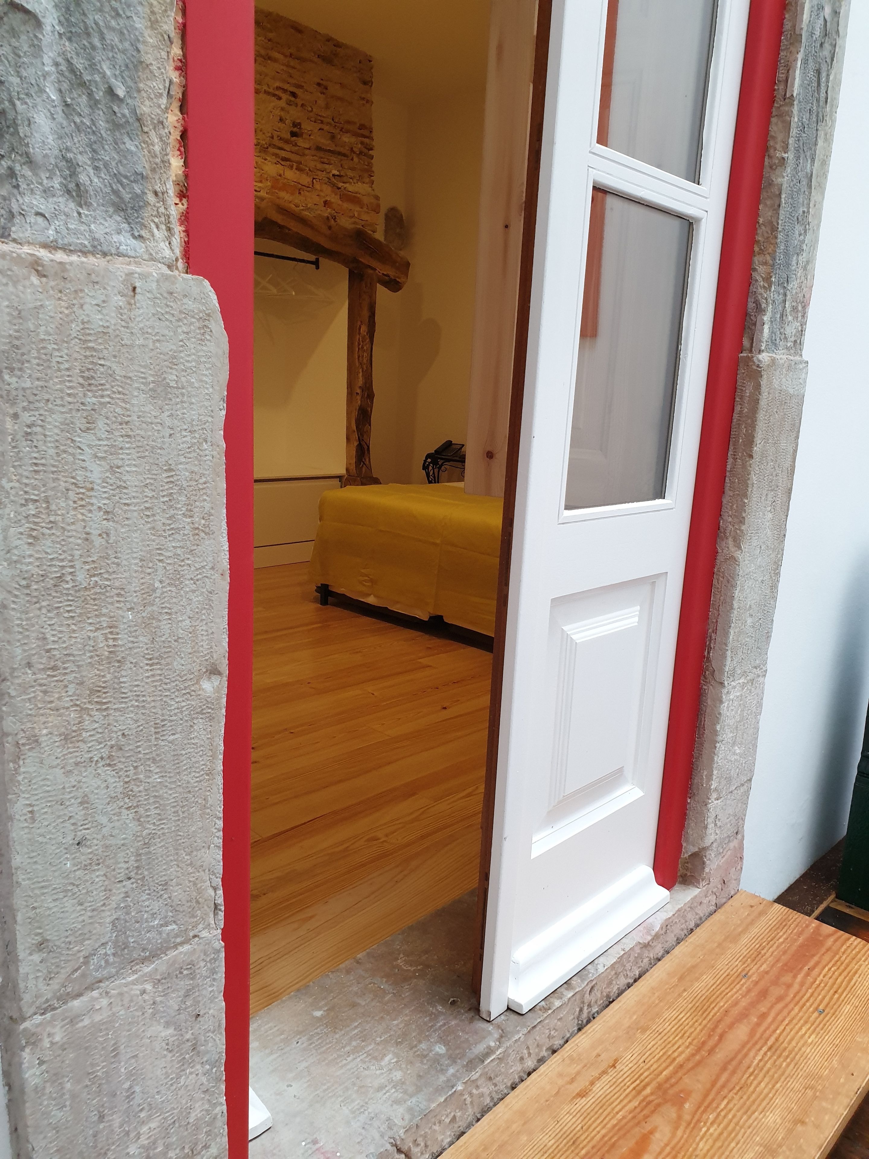 A room with a wooden floor, a yellow bed, and a red wall.