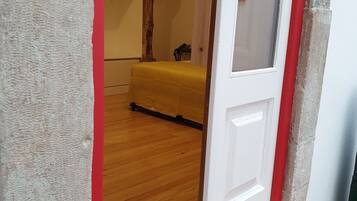 A room with a wooden floor, a yellow bed, and a red wall.