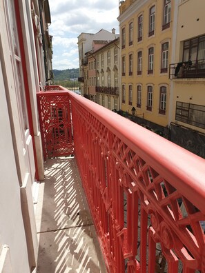 Un balcon avec une balustrade rouge donnant sur une rue bordée d’immeubles.
