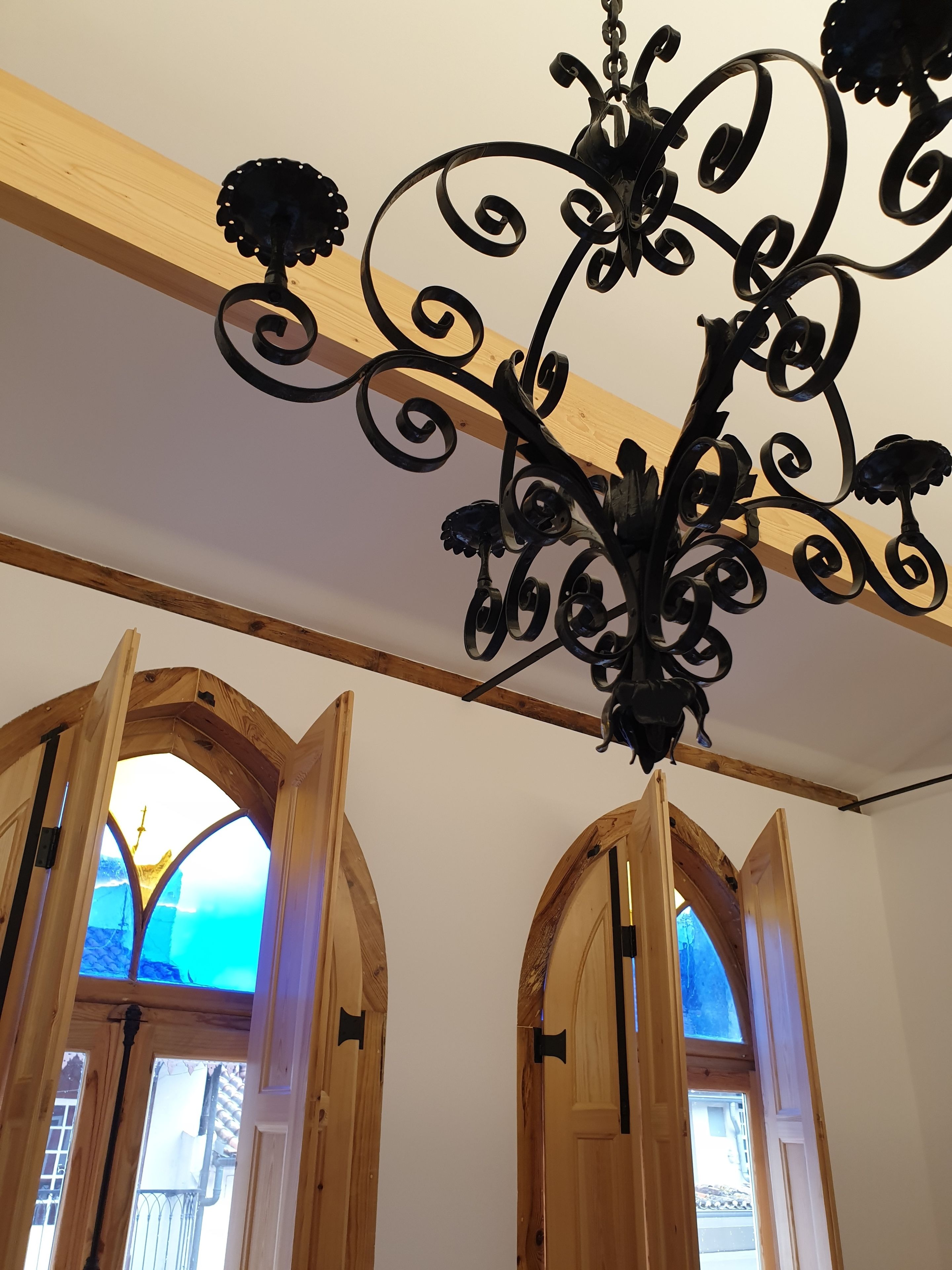 Un candelabro con detalles metálicos intrincados, vigas de madera y ventanas arqueadas que dan vista a un edificio.