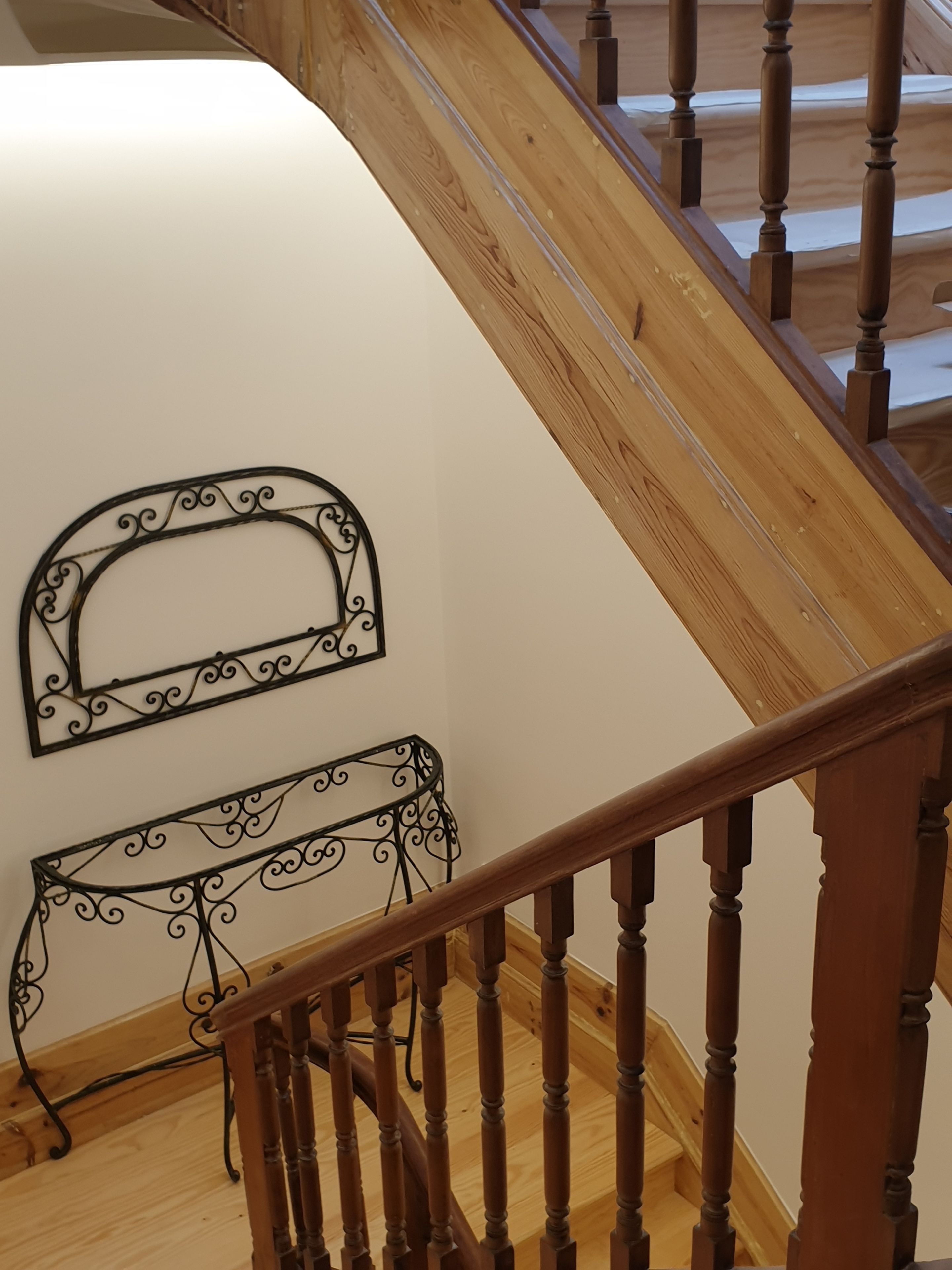 Un escalier en bois avec une rampe et un mur blanc orné de deux cadres métalliques décoratifs.