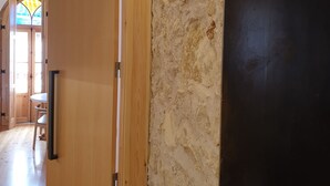 A hallway with a wooden door, a stone wall, and a view into another room with a round table and chairs.