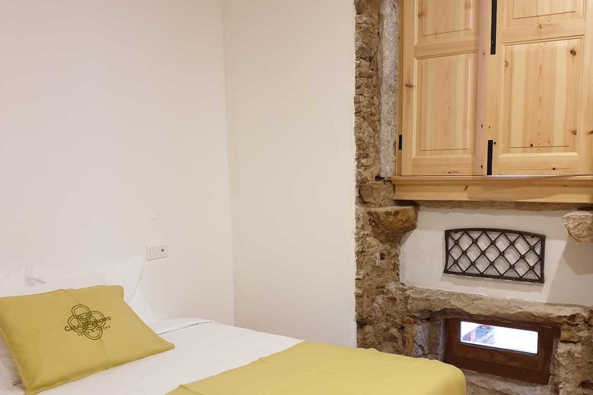 Une chambre à coucher avec un lit, une couvre-lit jaune, un mur en pierre, des armoires en bois et une petite fenêtre.