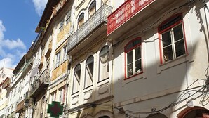 A row of historic buildings with balconies, some with red railings, and a cobblestone street.
