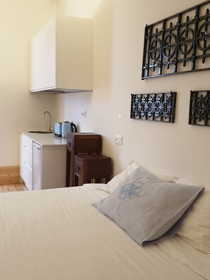 Une pièce de taille modeste comprenant un lit, une petite kitchenette et des éléments décoratifs en métal fixés au mur.