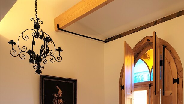 A bedroom with a bed, a chandelier, a wooden door, and a framed picture on the wall.