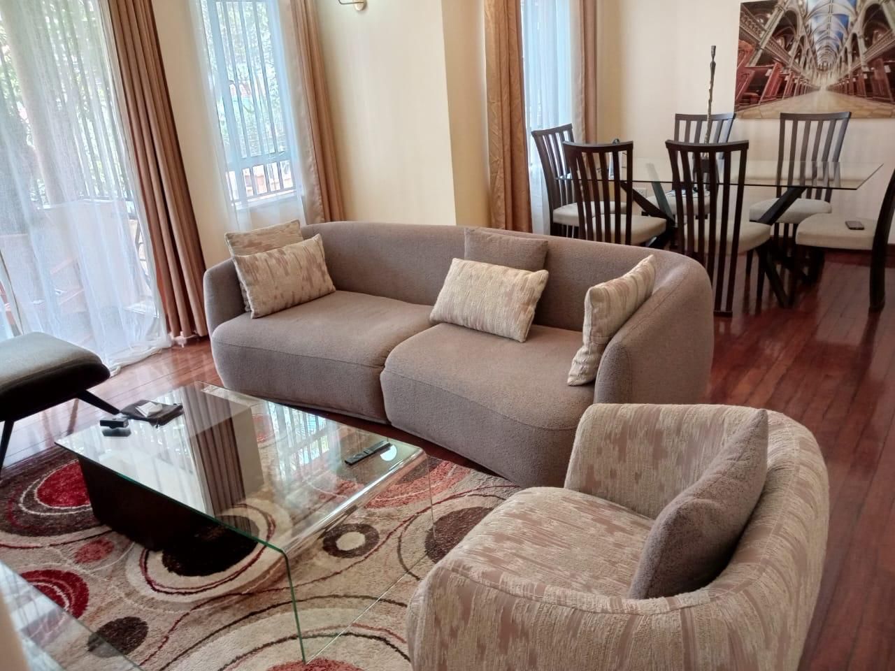 A living room with a sofa, armchairs, a glass coffee table, and a dining area with chairs and a table.