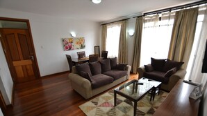 A living room with a wooden floor, two sofas, a coffee table, and a dining table with chairs. - Lighthomez Angles Heights (Nairobi)