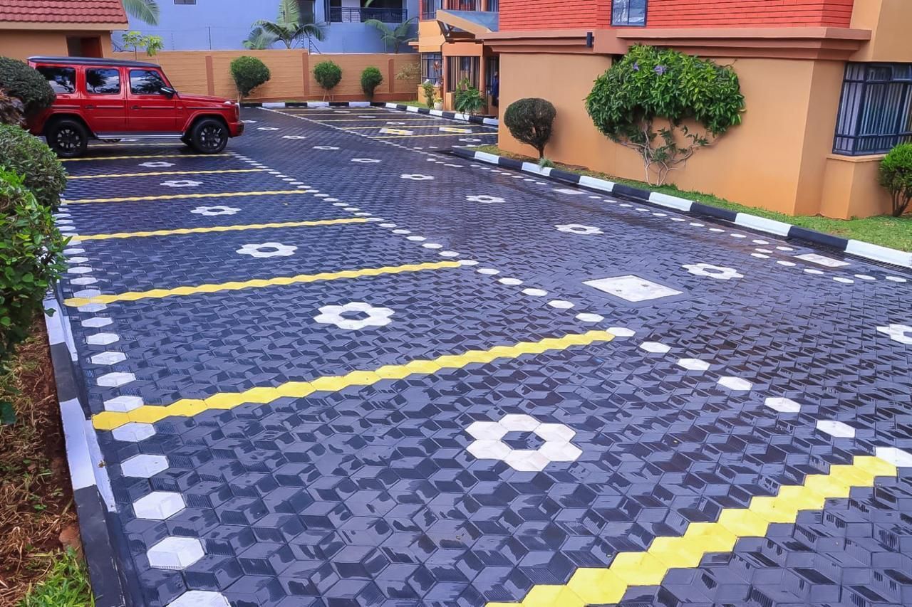 Um espaço de estacionamento com piso padronizado, um veículo vermelho e um edifício com telhado vermelho.