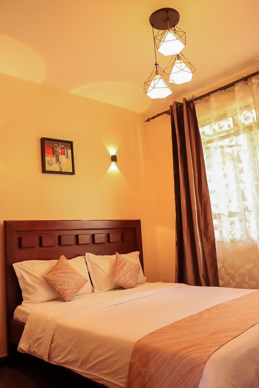 Quarto de hotel com cama, luminária na parede e janela com cortinas.