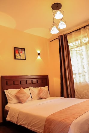 Quarto de hotel com cama, luminária na parede e janela com cortinas.