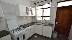 A kitchen with white cabinets, a gas stove, a sink, and a trash bin. - Lighthomez Angles Heights (Nairobi)