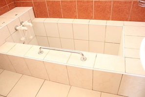 Una bañera con barra de apoyo, toallero y ducha.