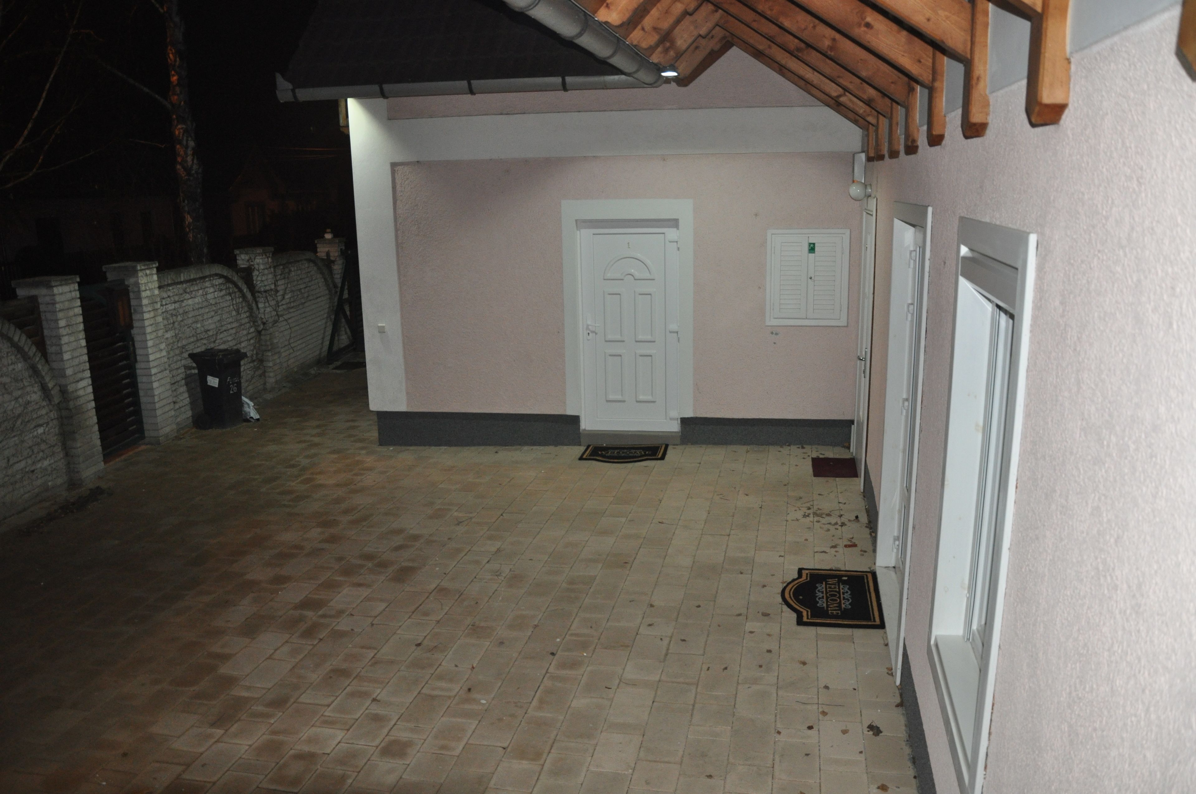 A covered outdoor area with a brick floor, a white door, and a window with a shutter.