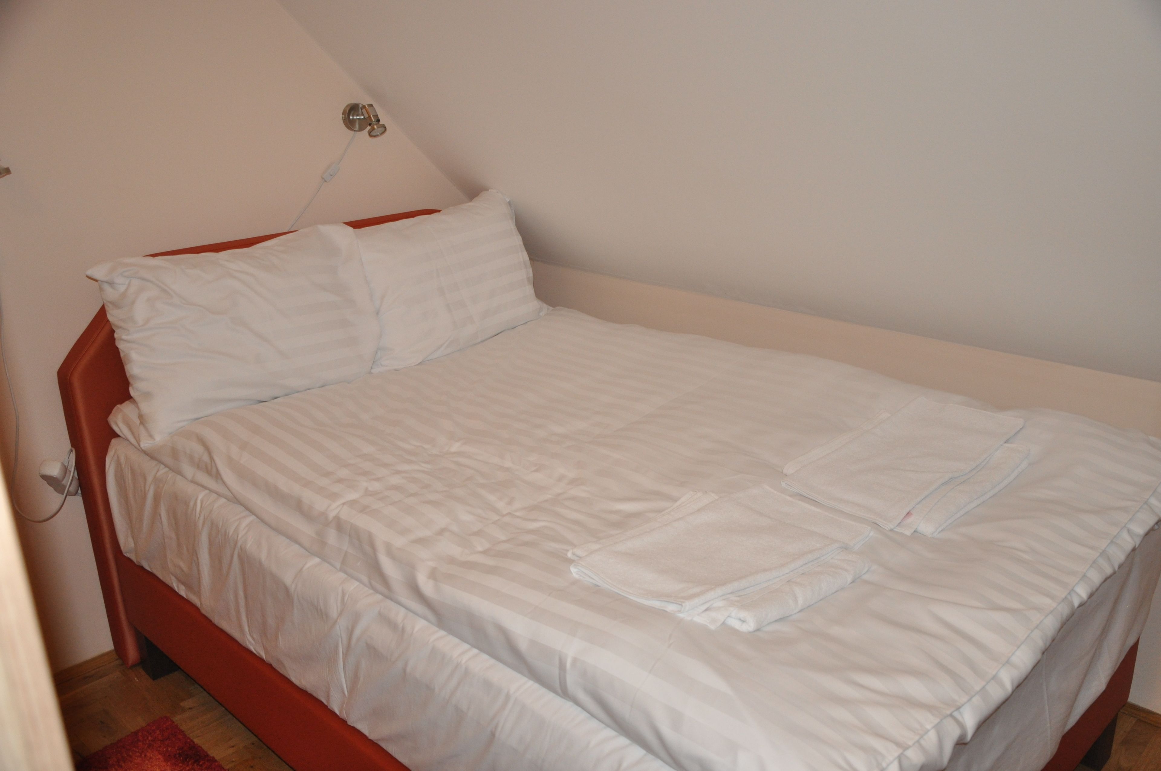 A single bed with white bedding in a room with a sloped ceiling and a red wall.