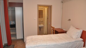 Ein Schlafzimmer mit Bett, Nachttisch, Stuhl und einem durchgehenden Türspalte sichtbaren Badezimmer.