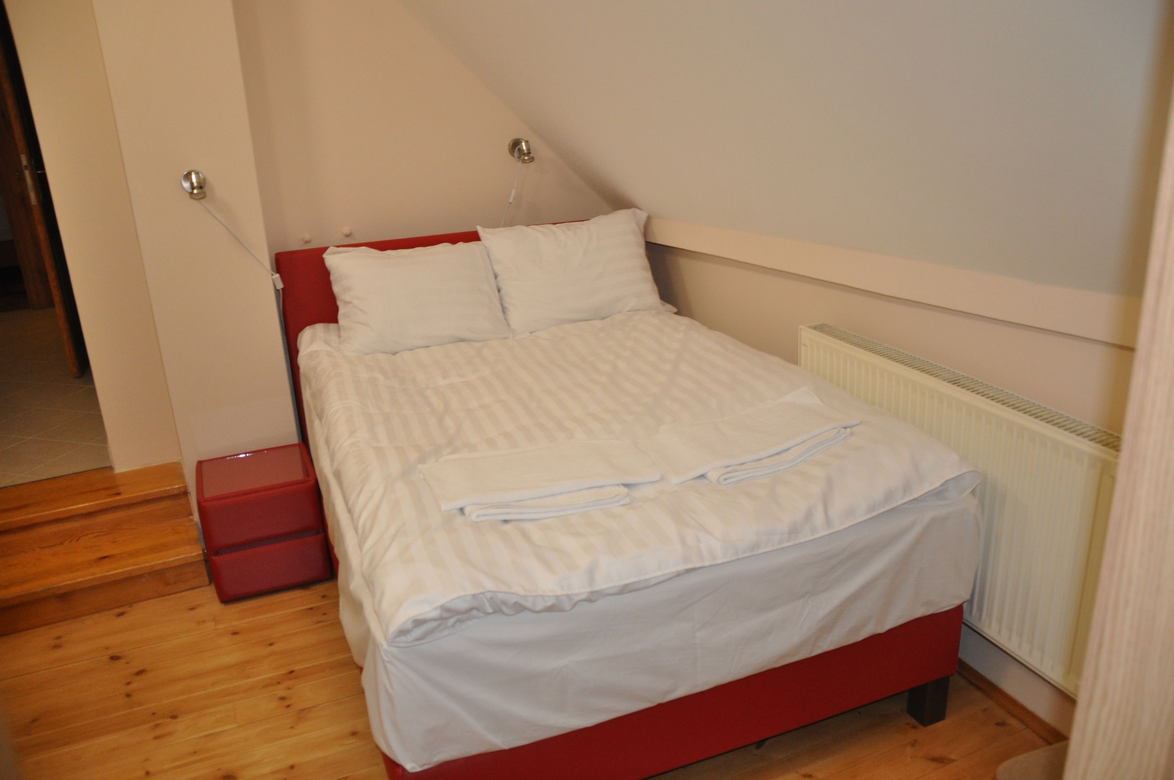 Una cama bien hecha con ropa blanca y un cabecero rojo en una habitación con piso de madera y un radiador blanco.