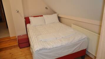 Una cama bien hecha con ropa blanca y un cabecero rojo en una habitación con piso de madera y un radiador blanco.