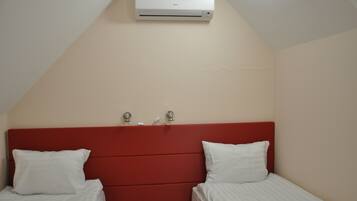 A bedroom with a red headboard, two single beds, white bedding, and an air conditioning unit mounted on the wall.