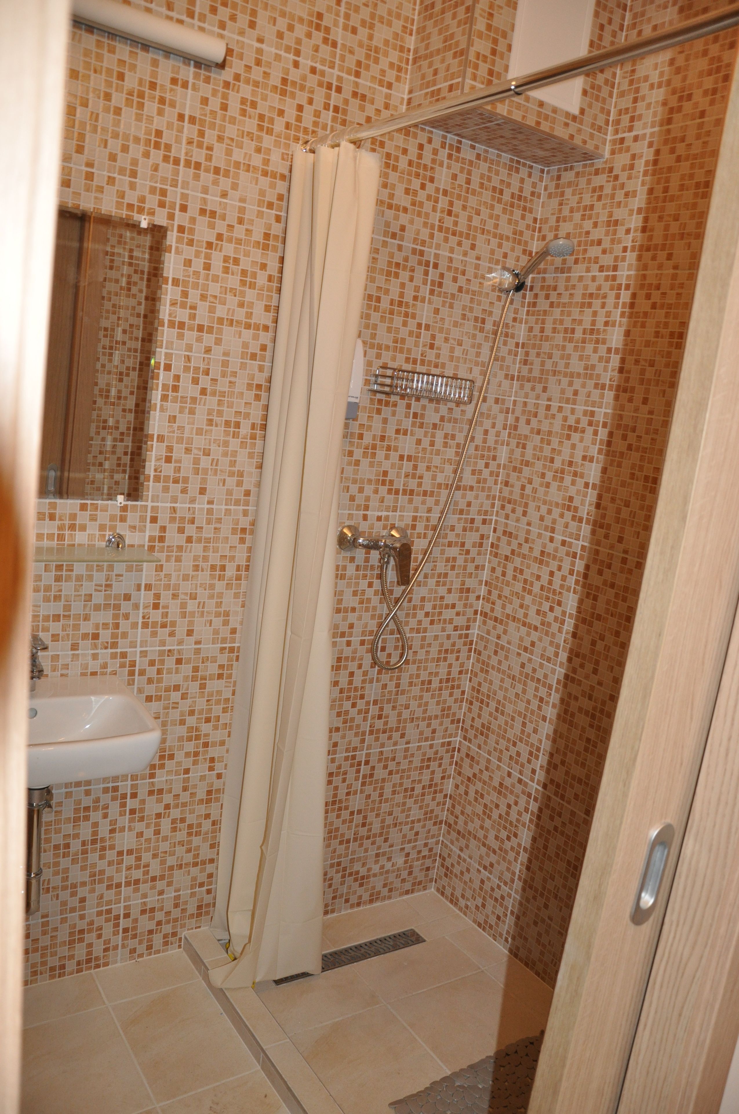 Een badkamer met wandtegels in mozaïek, een douche met glazen deur en een wastafel met spiegel.