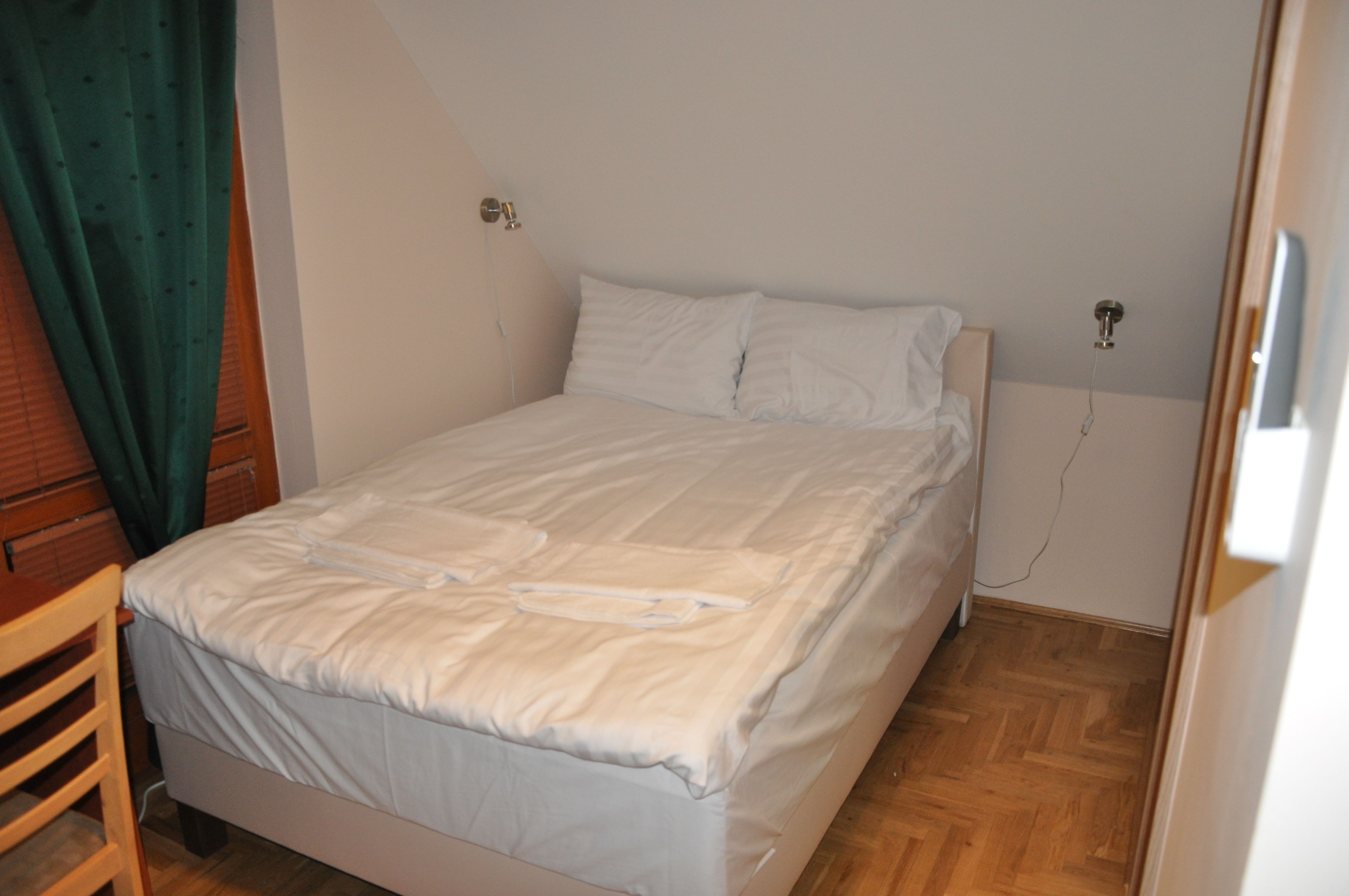 Una cama pequeña y bien hecha en una habitación con piso de madera y una cortina verde.