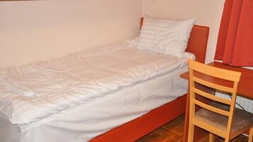 A single bed with a wooden headboard, a wooden chair, and a small table with a mirror above it.