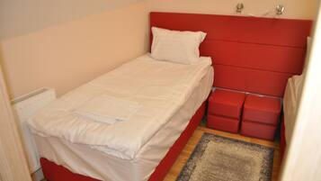 Une petite chambre avec un lit simple, dotée d’une tête de lit rouge et de linge de lit blanc.