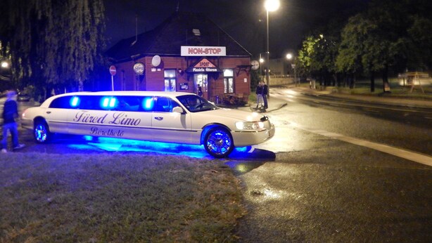 Eine weiße Limousine mit blauer Beleuchtung steht nachts auf einer Straße.