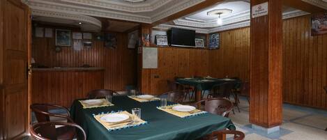 Un comedor con una larga mesa dispuesta para seis comensales, paneles de madera en las paredes y un techo con diseños elaborados.