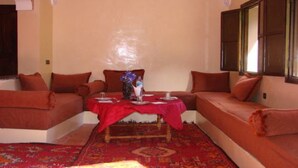 Una habitación con alfombra roja, dos sofás, una mesita con un jarrón y una ventana con contraventanas de madera.