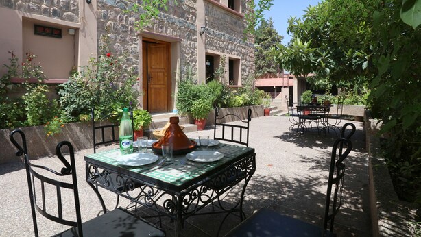 Un espacio de comedor al aire libre con una mesa dispuesta para dos personas, rodeado de muros de piedra y plantas en macetas.