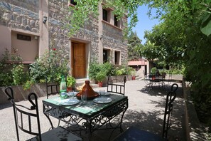 Un espace extérieur aménagé pour prendre les repas, avec une table dressée pour deux personnes, entouré de murs en pierre et de plantes en pot.