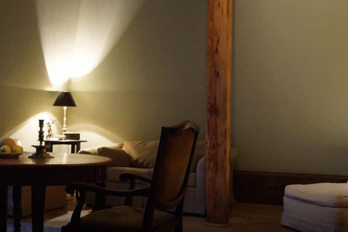 Una habitación tenuemente iluminada con un pilar de madera, una mesa con lámpara y un sofá.
