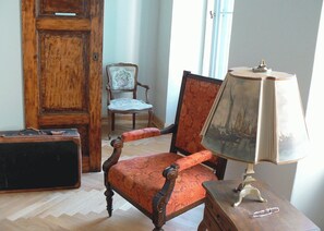 A room with a wooden door, a vintage chair, a table with a lamp, and a suitcase. - Schloss Lanke (Wandlitz)