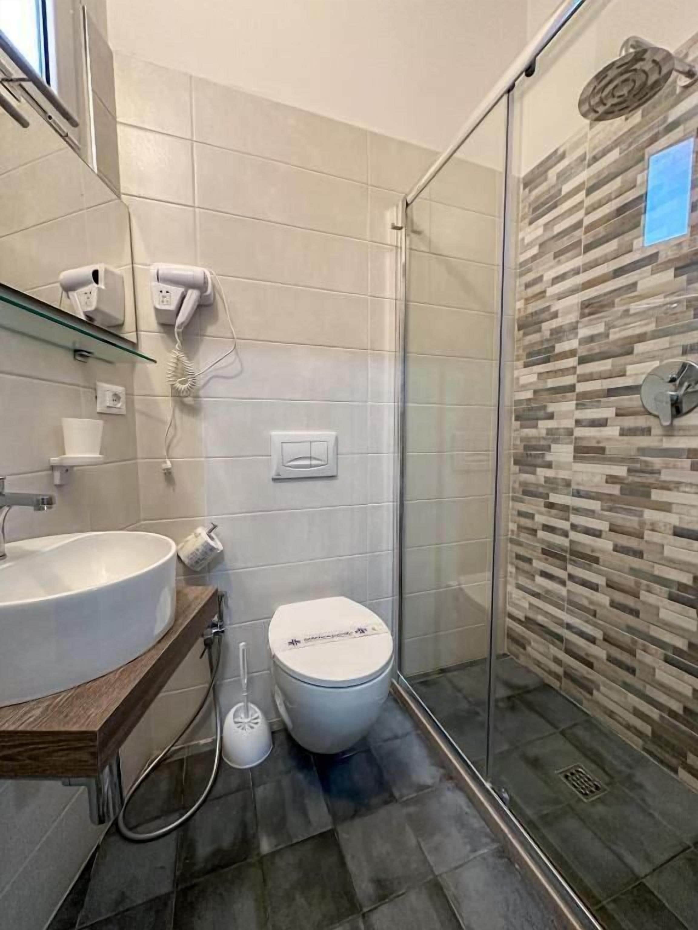 Een badkamer met een douchecabine van glas, een wastafel, toilet en spiegel.